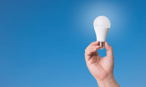 Hand holding LED Bulb with Lighting on blue sky background.