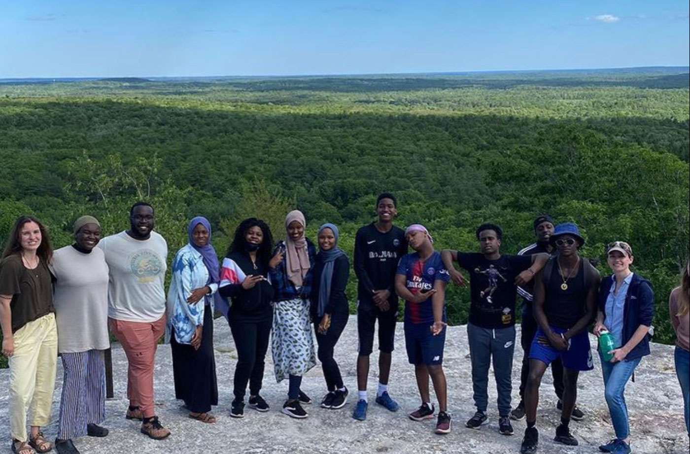 students on mountaintop with sky and trees behind them