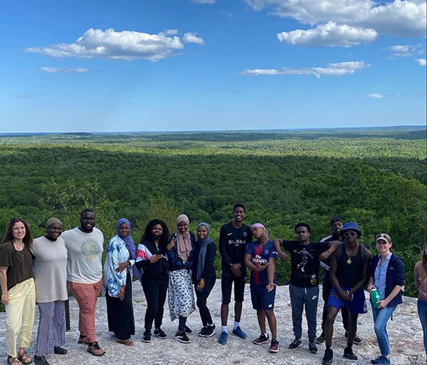 students on mountaintop with sky and trees behind them