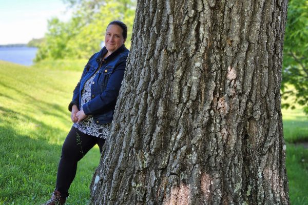 woman leaning against tree near lake