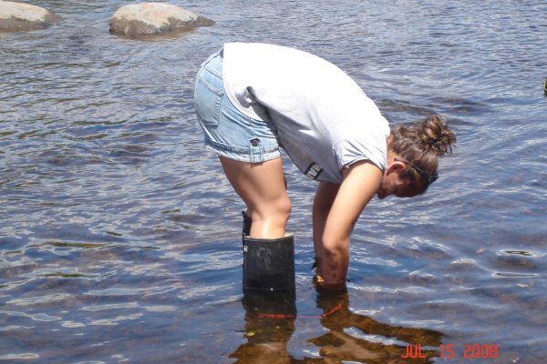 young woman bent over reaching for mussels in the Sebasticook River