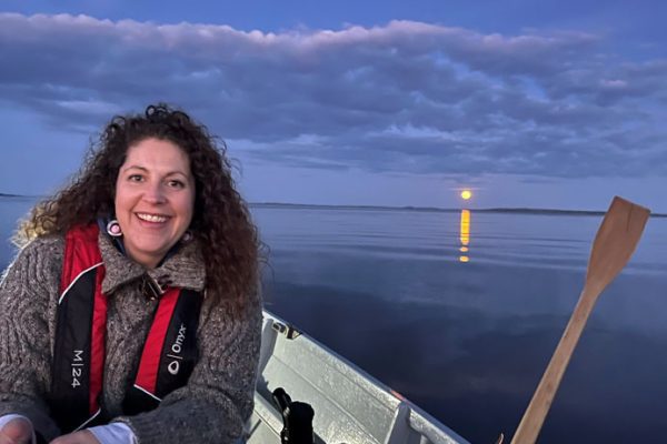 Woman on rowing boat in the bay with a full moon in the background