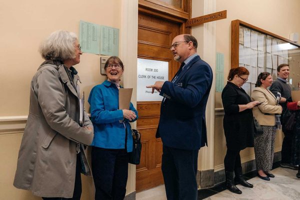 Two women speaking with man in hallway of State House