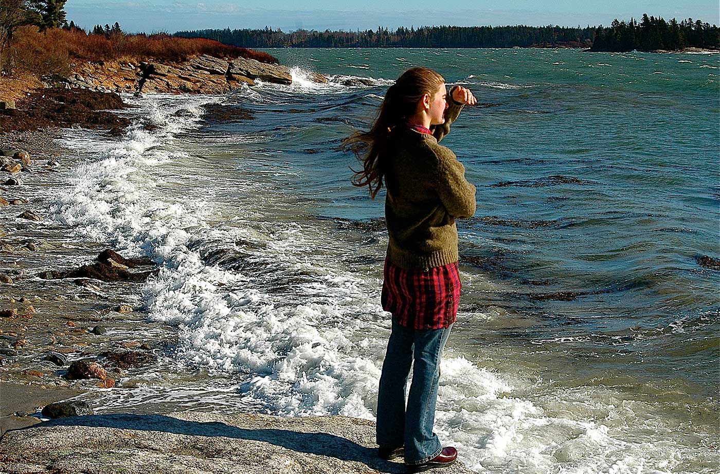young woman standing in ocean waves looking out at ocean