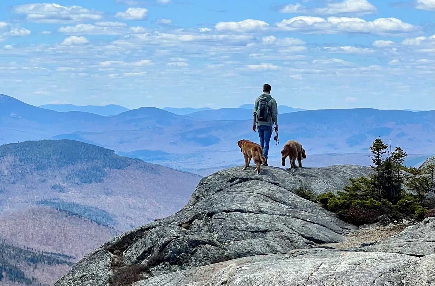 Young man and two dogs on top of mountain looking out at other mountains
