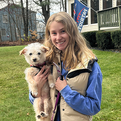 Hannah holding her dog in front of a New England Patriots flag