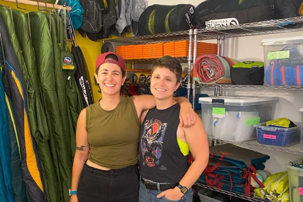 Owners standing in front of sleeping bags and outdoor gear.