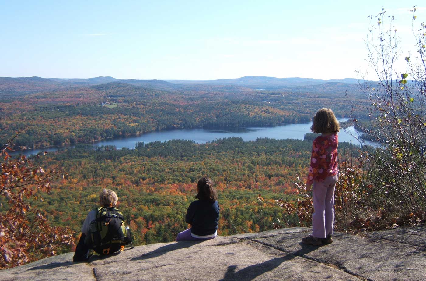 children sitting on top of mountain looking out at water and fall foliage