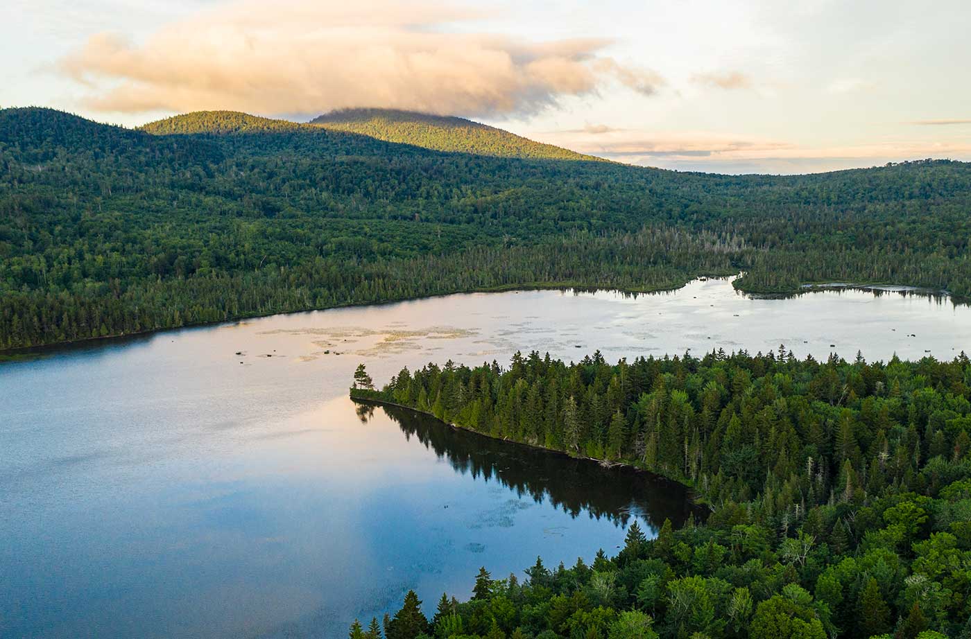 clouds over mountain with forests and pond in foreground