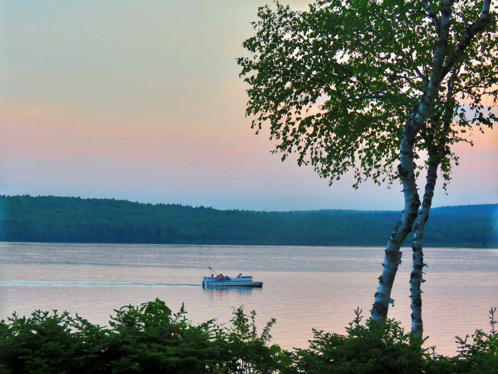 People in pontoon boat on lake at sunset