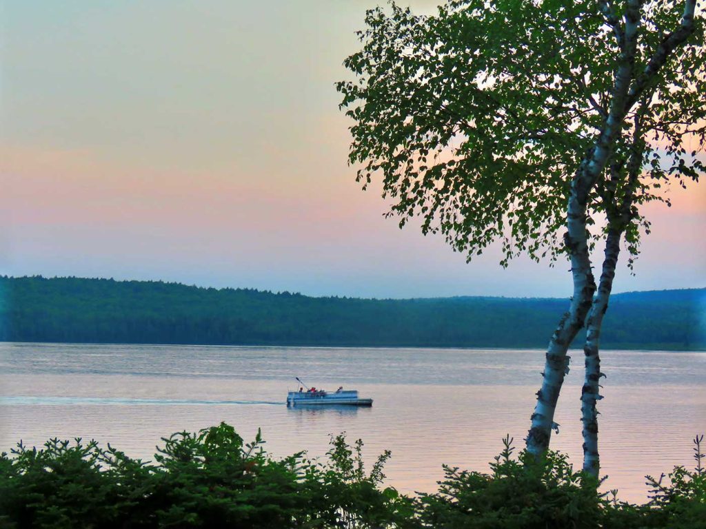 People in pontoon boat on lake at sunset