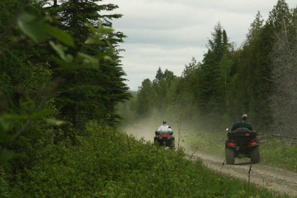 Twp people driving ATVs on dirt trail surrounded by trees