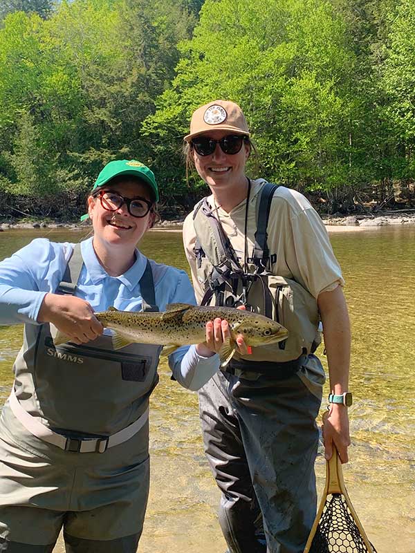 Young person holding fish standing with Keaton, both smiling