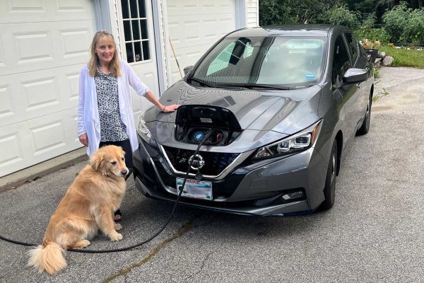 woman and her dog standing next to electric car being charged from home