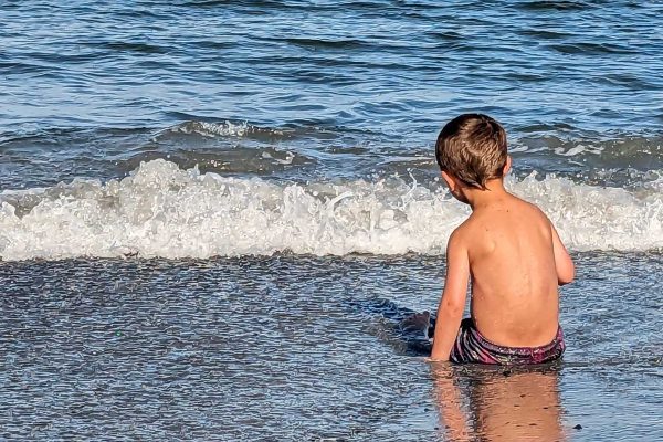 young boy sitting on beach by ocean wave