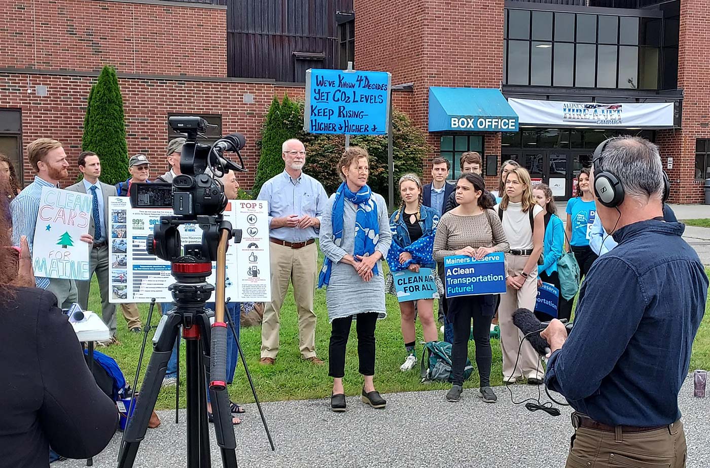 Person speaking in front of rally of people with signs