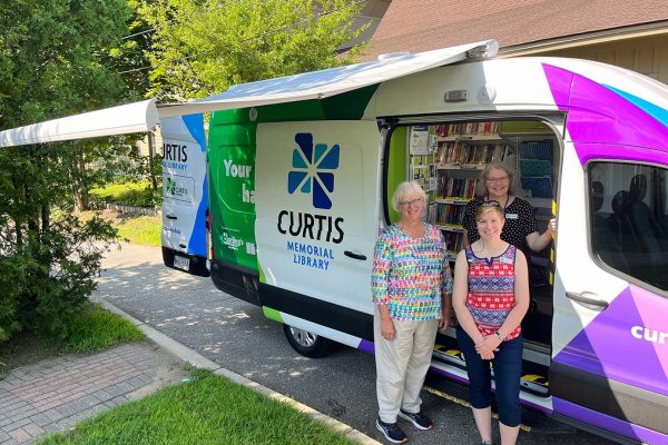 three women standing in front of electric van under awning