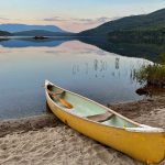 canoe on shore of Lobster Lake with mountains in background