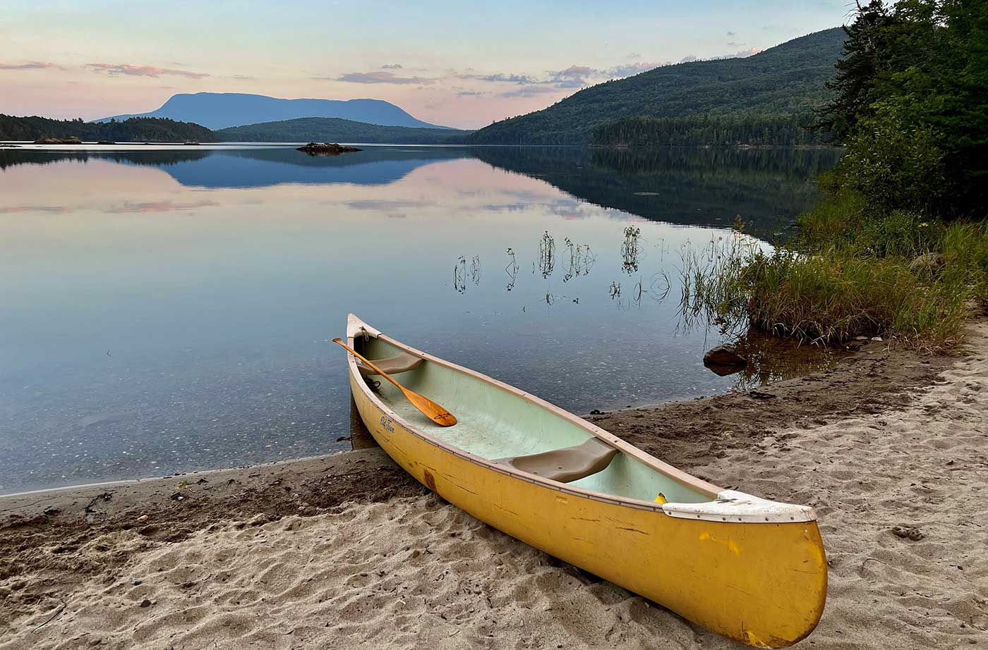 canoe on shore of Lobster Lake with mountains in background