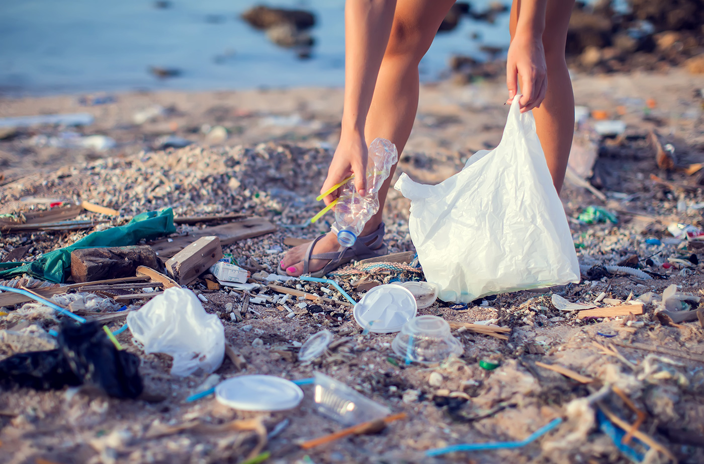 someone picking up plastic trash on a beach using a bag