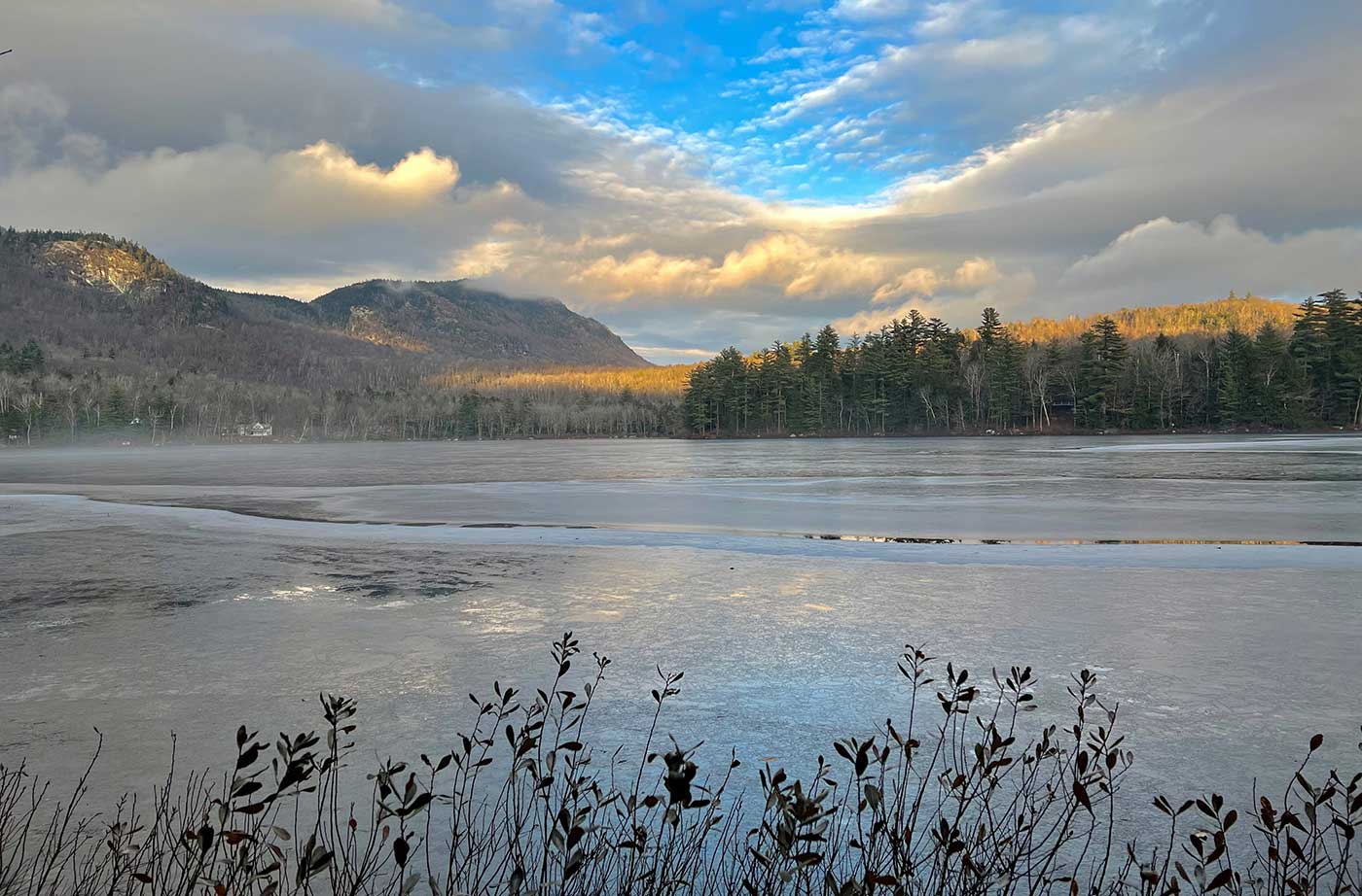 Two mountains behind pond, with lots of clouds and spot of blue sky