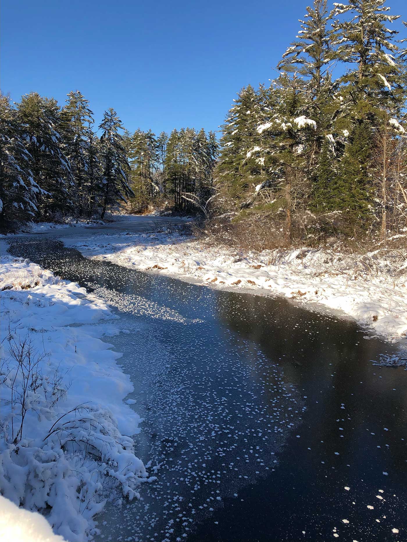 Calm stream of water surrounded by snowy banks and a bright blue sky