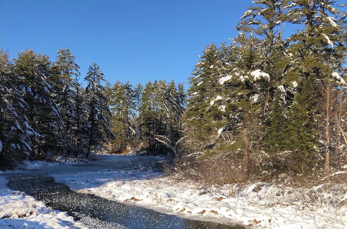 Calm stream of water surrounded by snowy banks and a bright blue sky