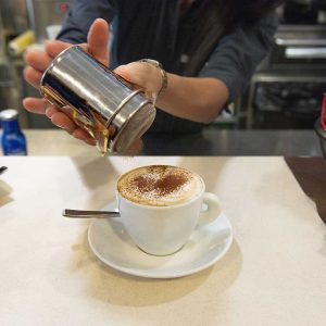 adding cinnamon to top of hot beverage in reusable porcelain mug