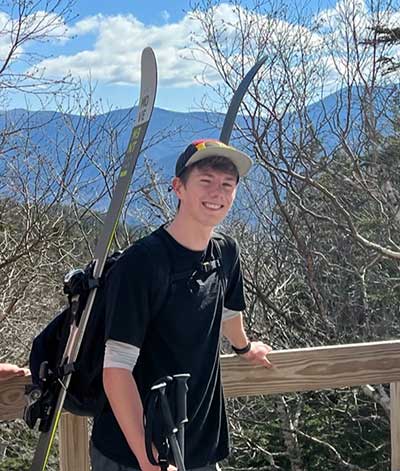 young man standing with skis in front of mountain view