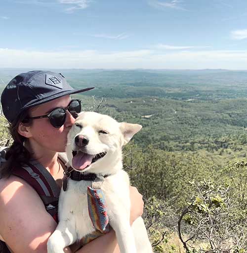 Sierra holding her dog while sitting atop a mountain