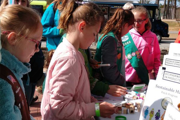 Girl Scouts looking at info about NRCM SM patch at outdoor table
