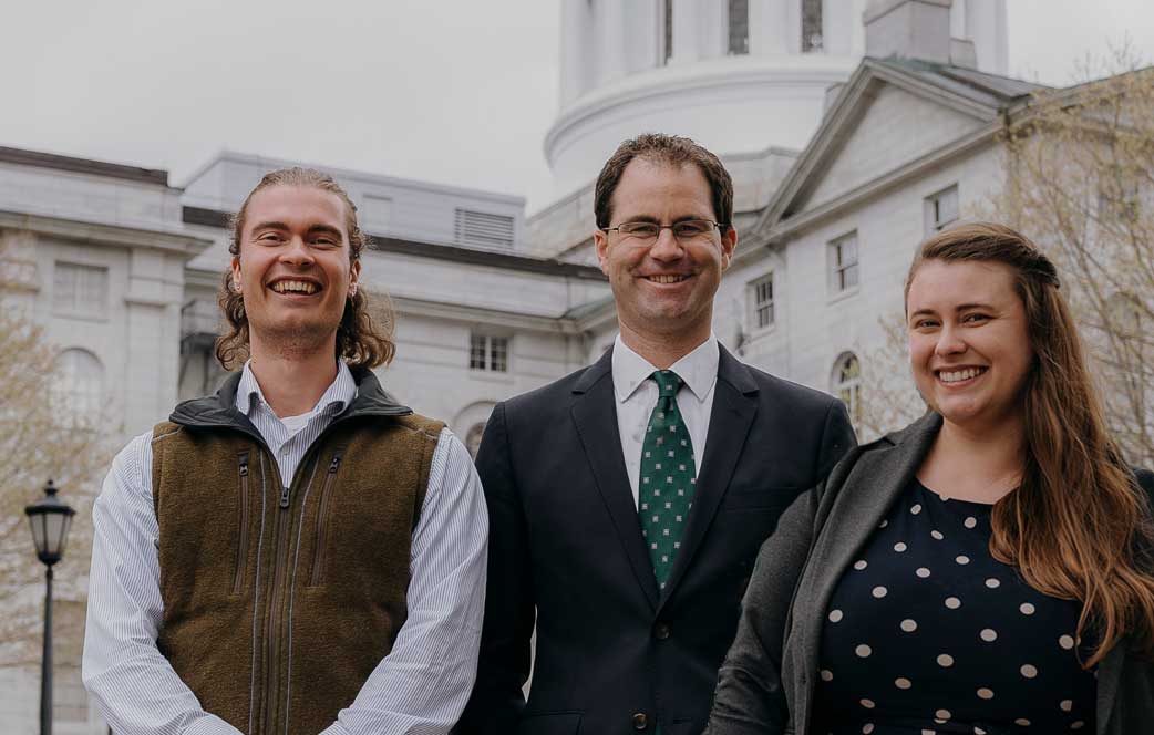 three people smiling and standing in front of State House