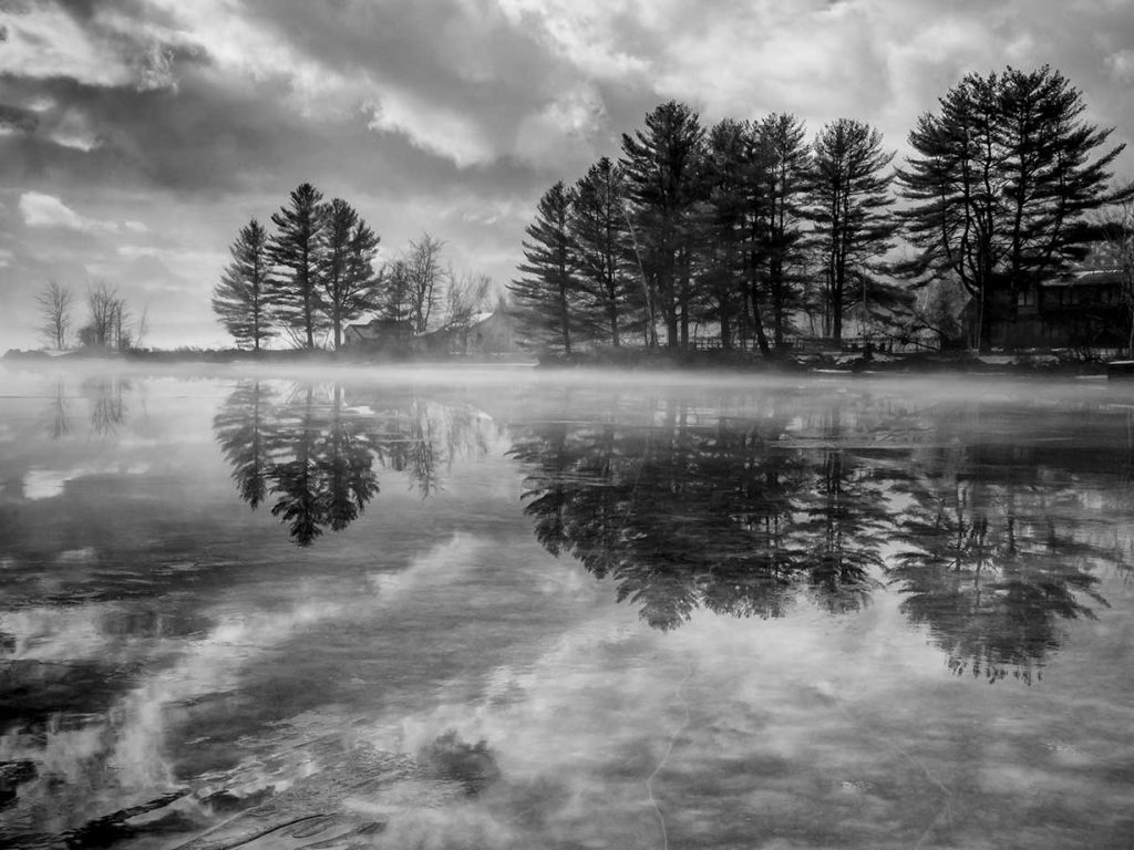 reflection of trees on lake with clouds behind trees