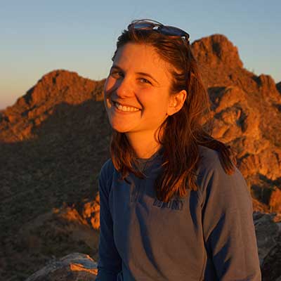 woman smiling in sunlight with mountains behind her