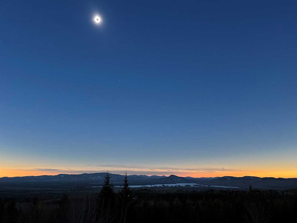 total solar eclipse in dark blue sky over lake