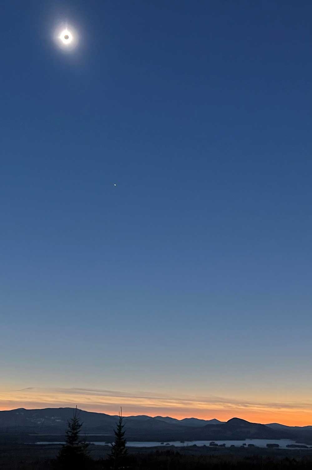 total eclipse over mountains and lake in dark blue sky