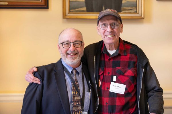 two men smiling, one has arm around the other