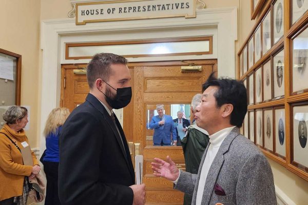 man wearing mask speaking with another man in hall of State House