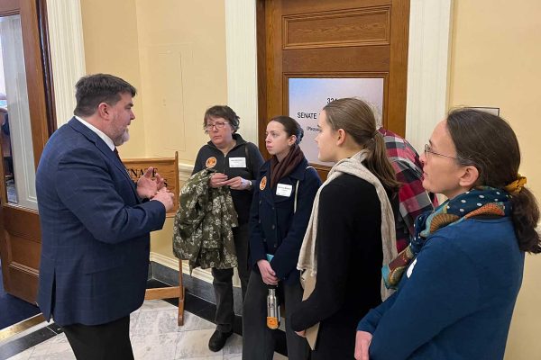 legislator speaking to group who are intently listening in hall of State House