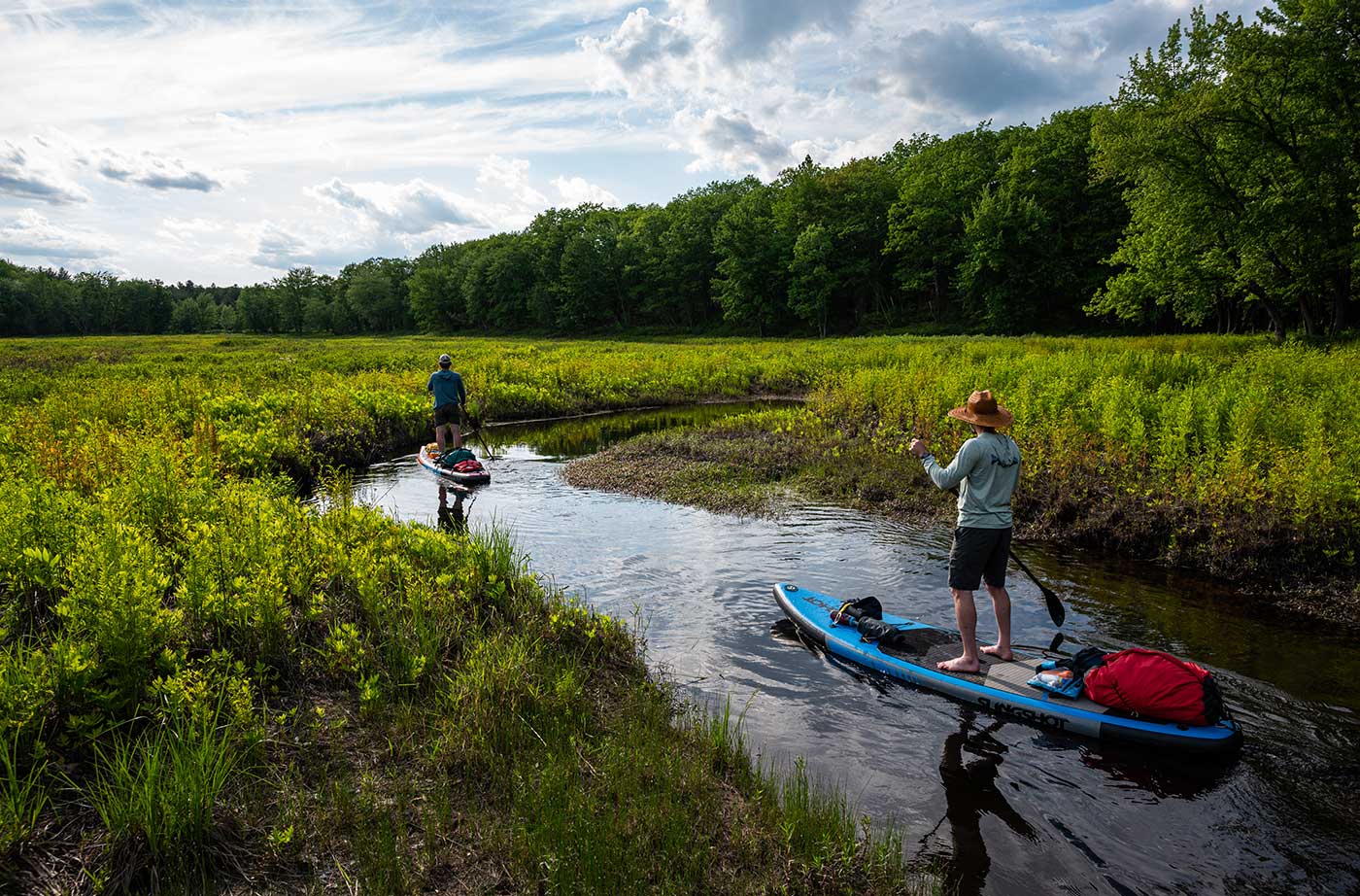 two people paddleboarding down river