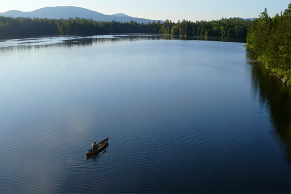 person canoeing in large lake with mountains and forests in background