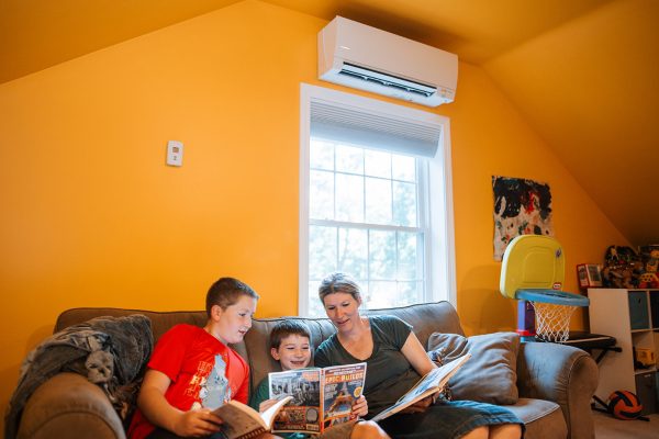Parent and children sitting on sofa looking at book, while sitting under a heat pump