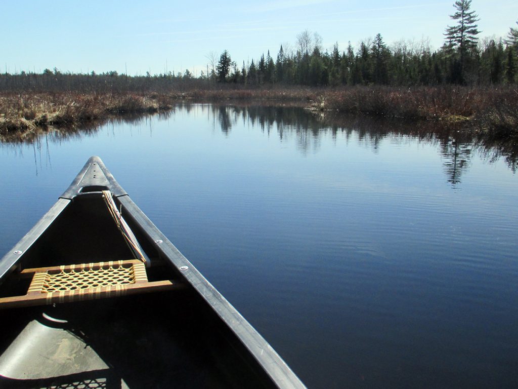 front of canoe headed down a calm waterway
