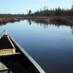 front of canoe headed down a calm waterway