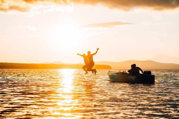 people jumping off boat into water at sunset