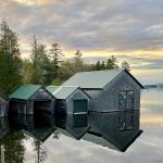 Boathouses on edge of water, with tall trees behind them