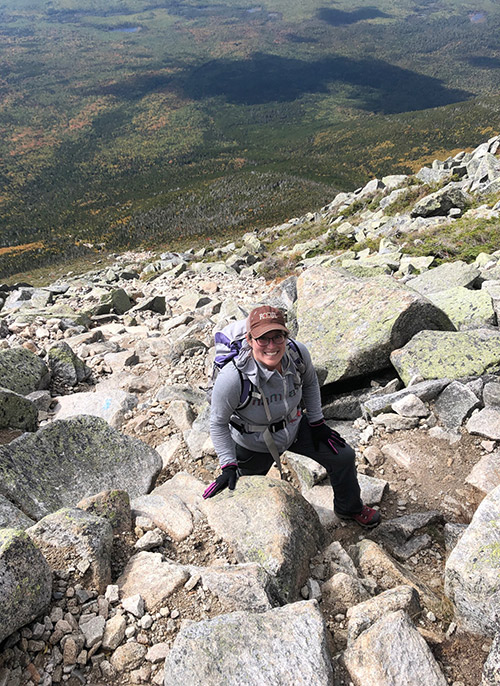 person on steep mountainside, smiling and looking up at camera