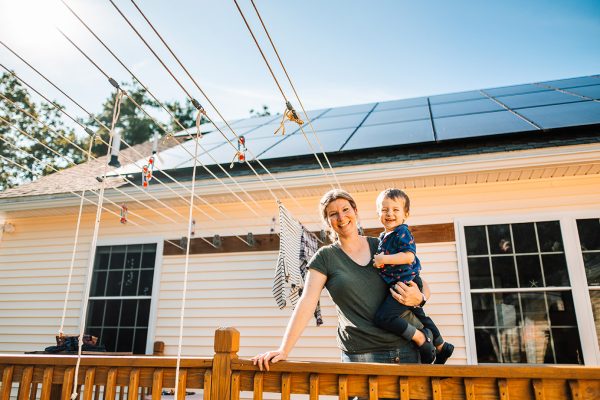 woman holding a small child in front of solar panels on roof and clothesline on deck