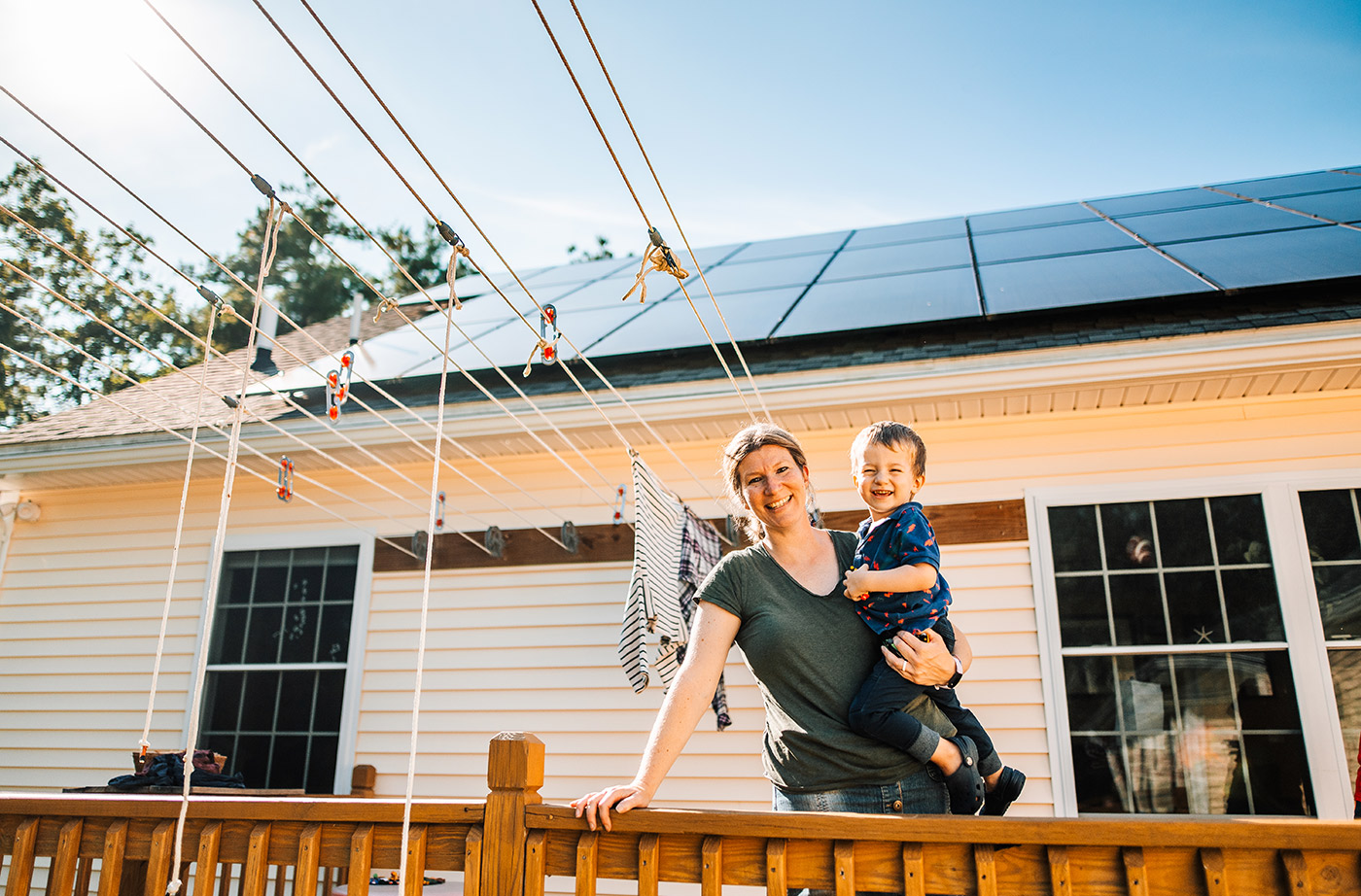 woman holding a small child in front of solar panels on roof and clothesline on deck