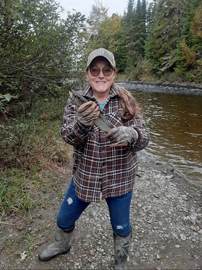 Woman smiling, holding a fish by a river